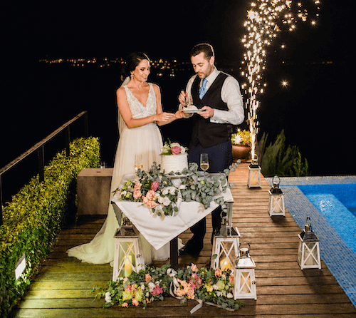 Couple cutting their wedding cake by the swimming pool in the evening